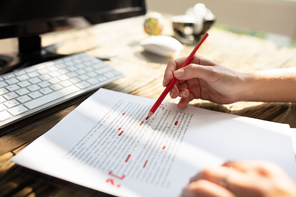 Hand of a person making notes and corrections with red ink on a physical sheet of paper