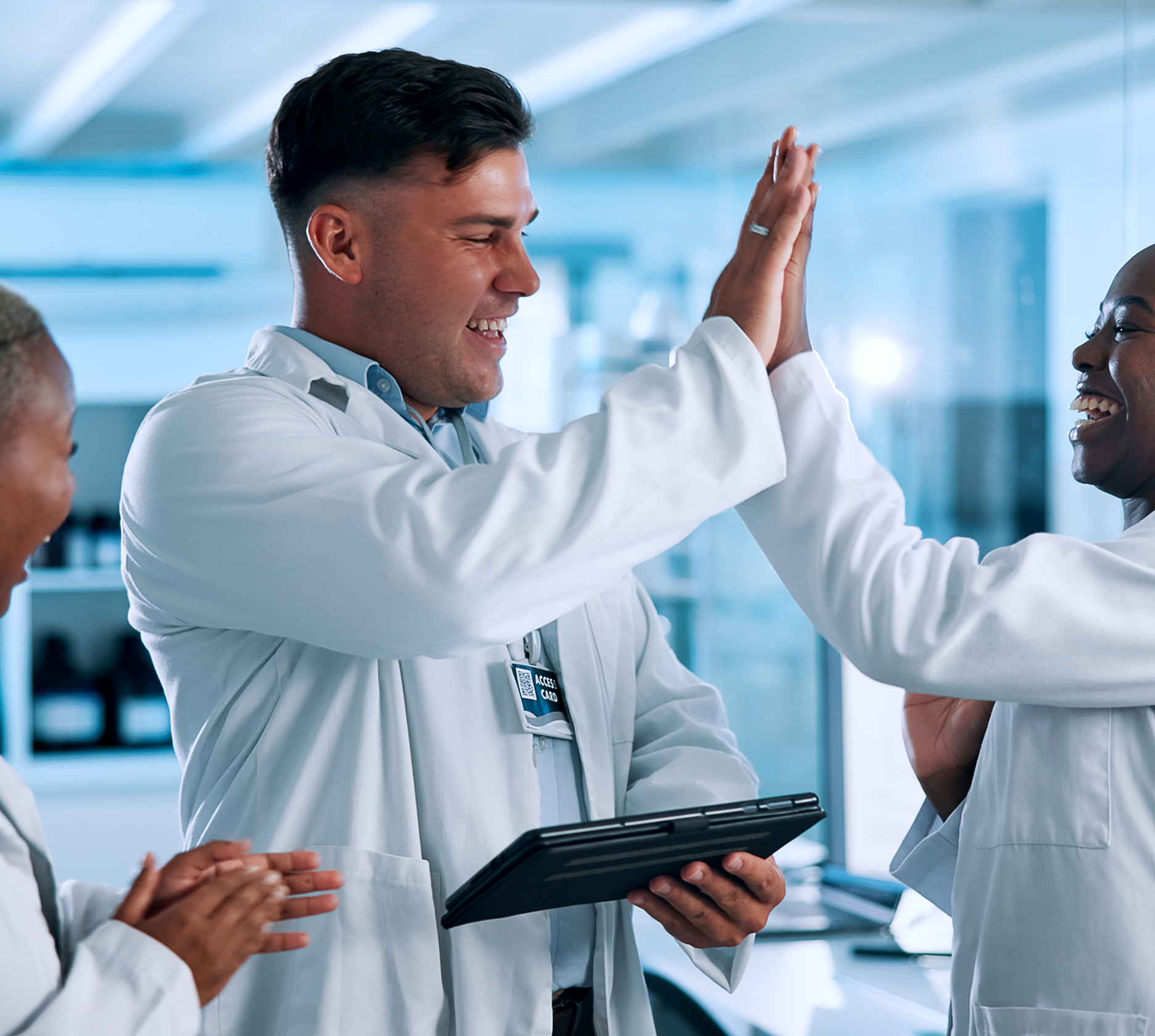 A man in a lab coat high-fives a woman in a lab coat while another claps